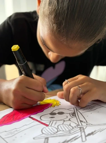 Nossa História Criança loira sentada à mesa pintando o Snoop.